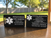 Two black medical ID tags on a wooden surface with trees and grass in the background.