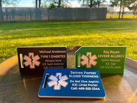 Three medical alert tags on a metal surface with a grassy field in the background