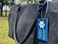Gray bag with a blue medical alert tag on a grassy background