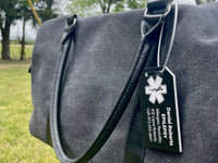 Gray bag with a black tag featuring a medical symbol and text, outdoors.