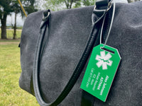 Gray bag with a green emergency tag attached, outdoors.