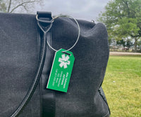 Green tag with a white emblem on a black bag outdoors