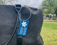 Blue medical ID tag on a gray bag with a grassy area and trees in the background