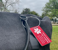 Red medical ID tag on a black bag with trees and grass in the background