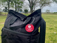 Black bag with a red tag featuring contact information on a grassy field background